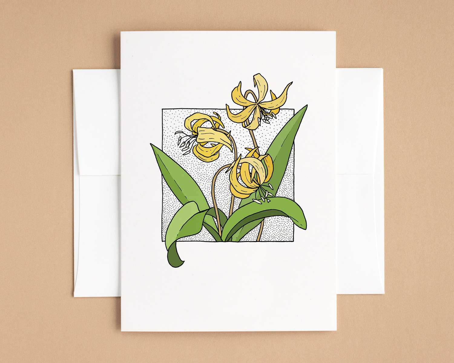 A vertical white card depicts a spray of yellow flowers surrounded by long spade-like leaves. The card sits on top of a white envelope, which lies on top of a brown backdrop.